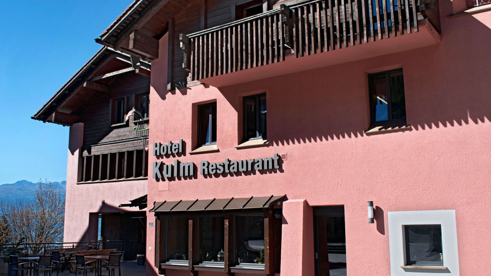 The pink facade of the Hotel Kulm restaurant with a wooden balcony in an alpine setting.