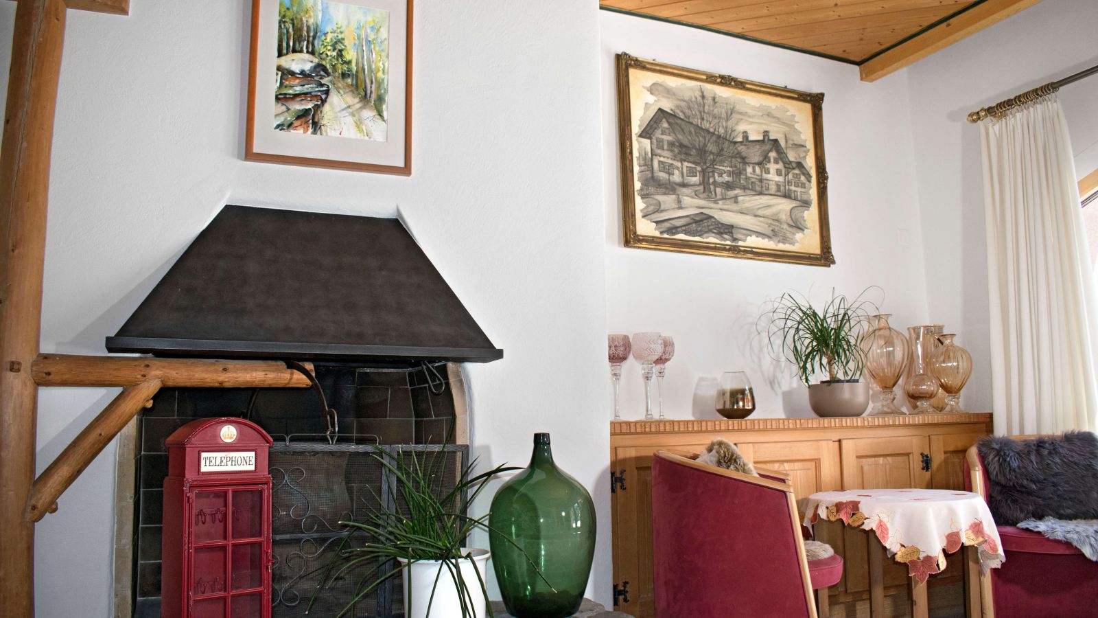 A fireplace area featuring a red telephone box, a green glass bottle, and two framed pictures on the wall.